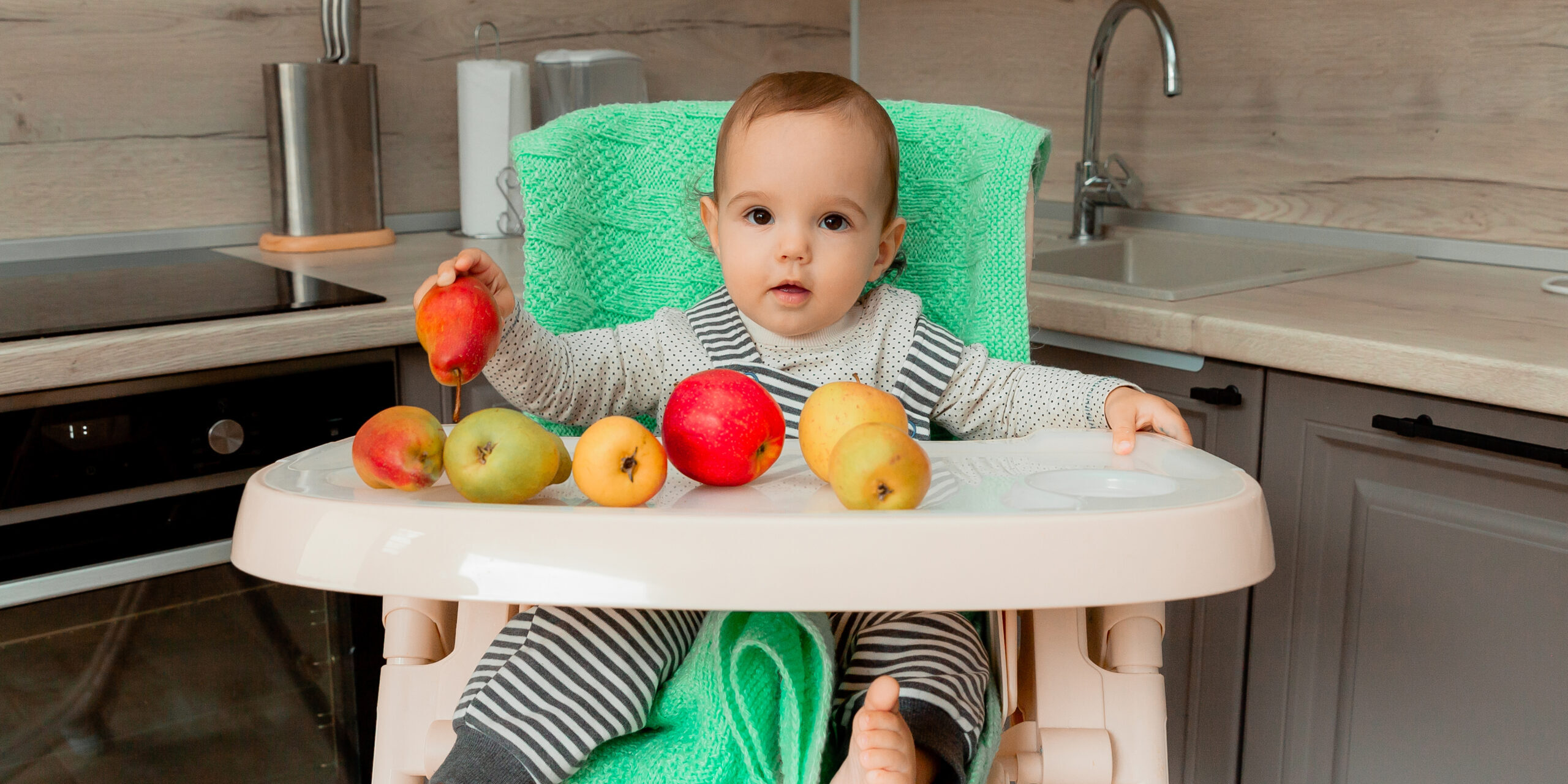 baby sits in a highchair and eats fruit.