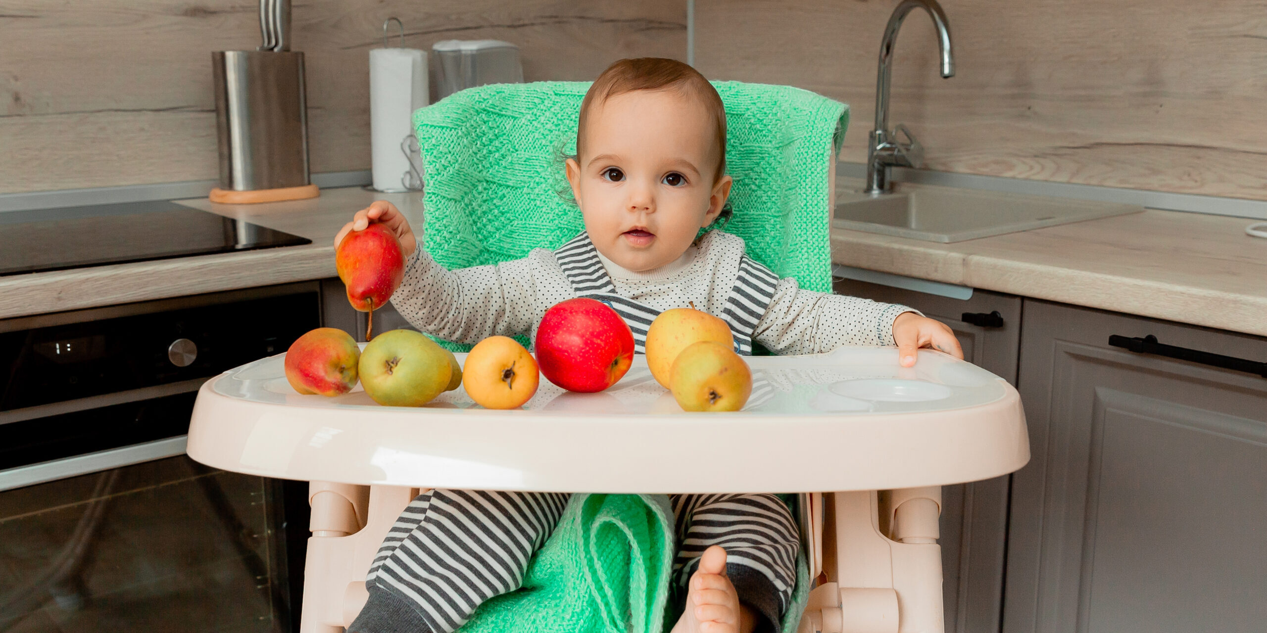 baby sits in a highchair and eats fruit. baby sits in a highchair and eats fruit.