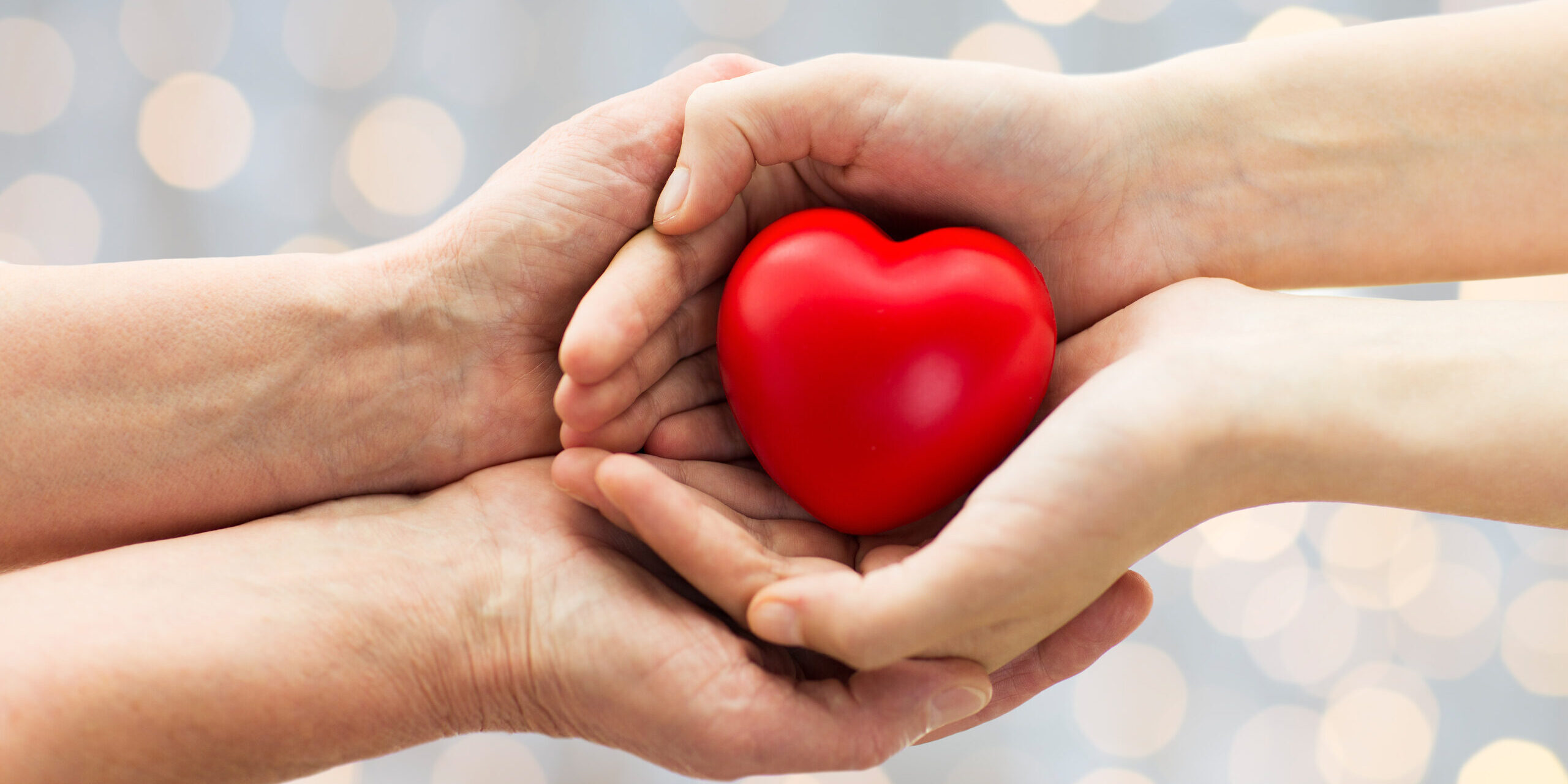 people, age, family, love and health care concept - close up of senior woman and young woman hands holding red heart over lights background