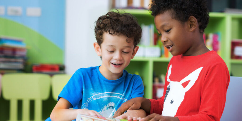 Student in international preschool reading a magazine book together in school library, education, kid and study concept