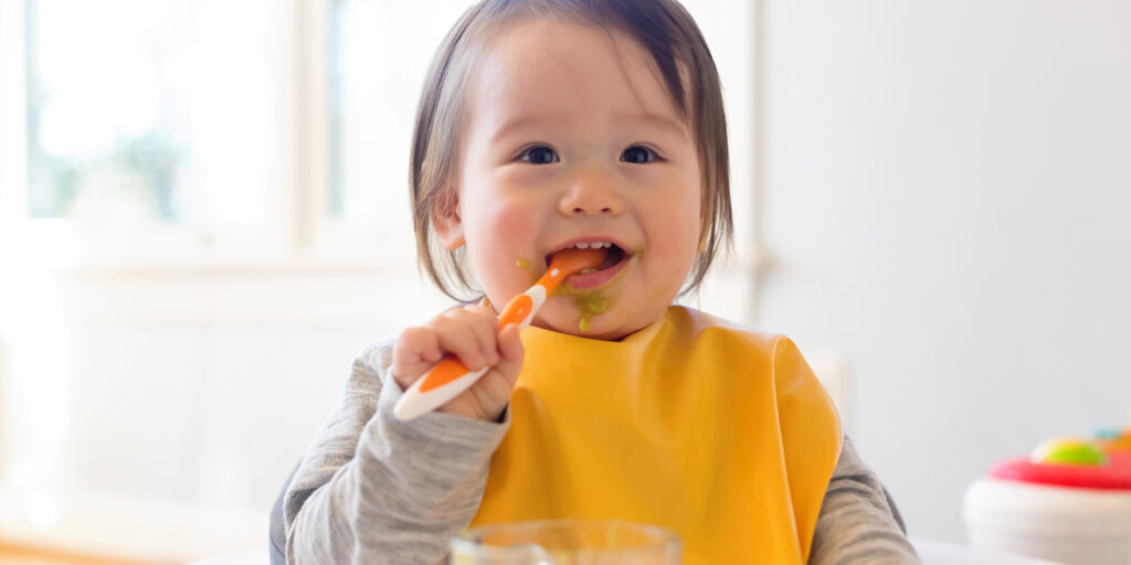 Happy little baby boy eating food in his house